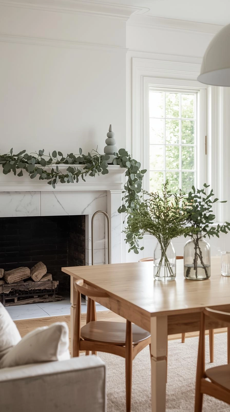 Minimalist Christmas decor with eucalyptus and pine garlands draped naturally across a mantel and table in a bright living room.